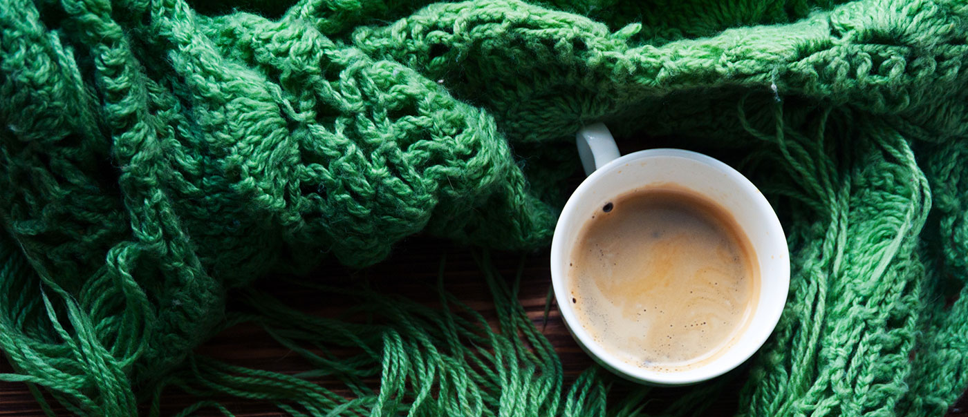 White coffee mug surrounded by a green blanket