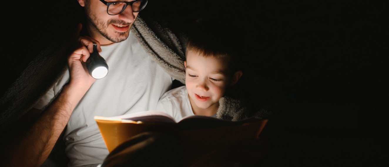 Dad and kid reading book by flashlight