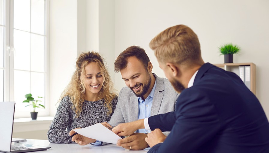 Couple smiling at document with real estate agent pointing