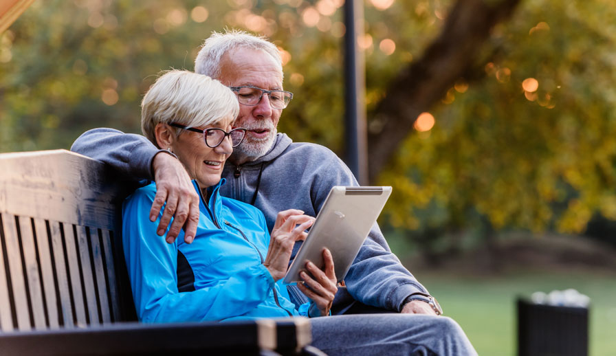 Couple looking at a tablet together on a bench.